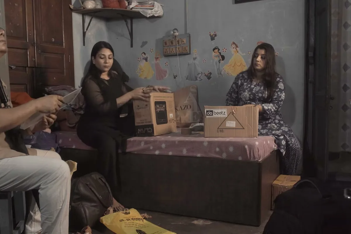 Two figures in a cluttered room hung with paper shapes, from Ek Mausiqi ka Dabba